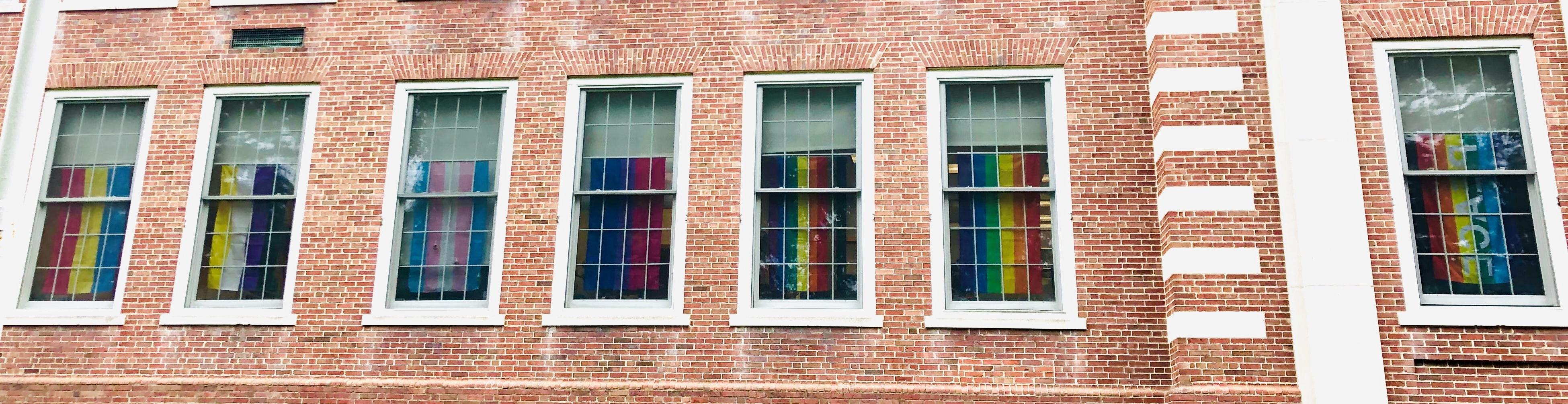 lgbtq pride flags in HR windows. from left to right: rainbow peace, rainbow, Philadelphia pride, bisexuality, transgender, nonbinary, pansexuality